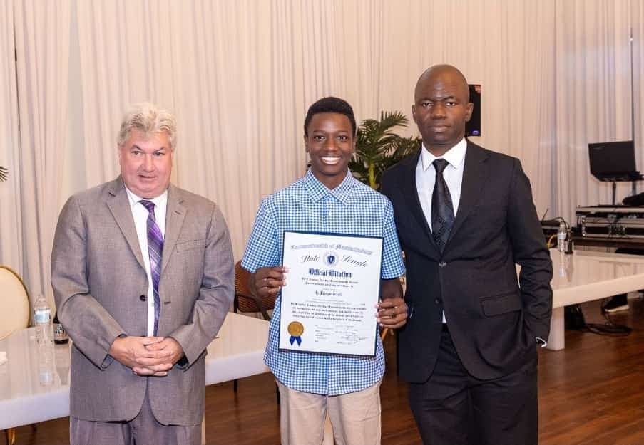 A young author holds his Official Citation with Senator Michael Brady and Charles Awodu.
