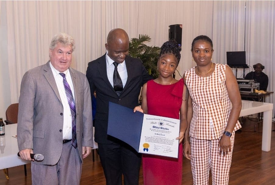 A young leader holds her Official Citation with Senator Michael Brady, Charles Awodu, and family.
